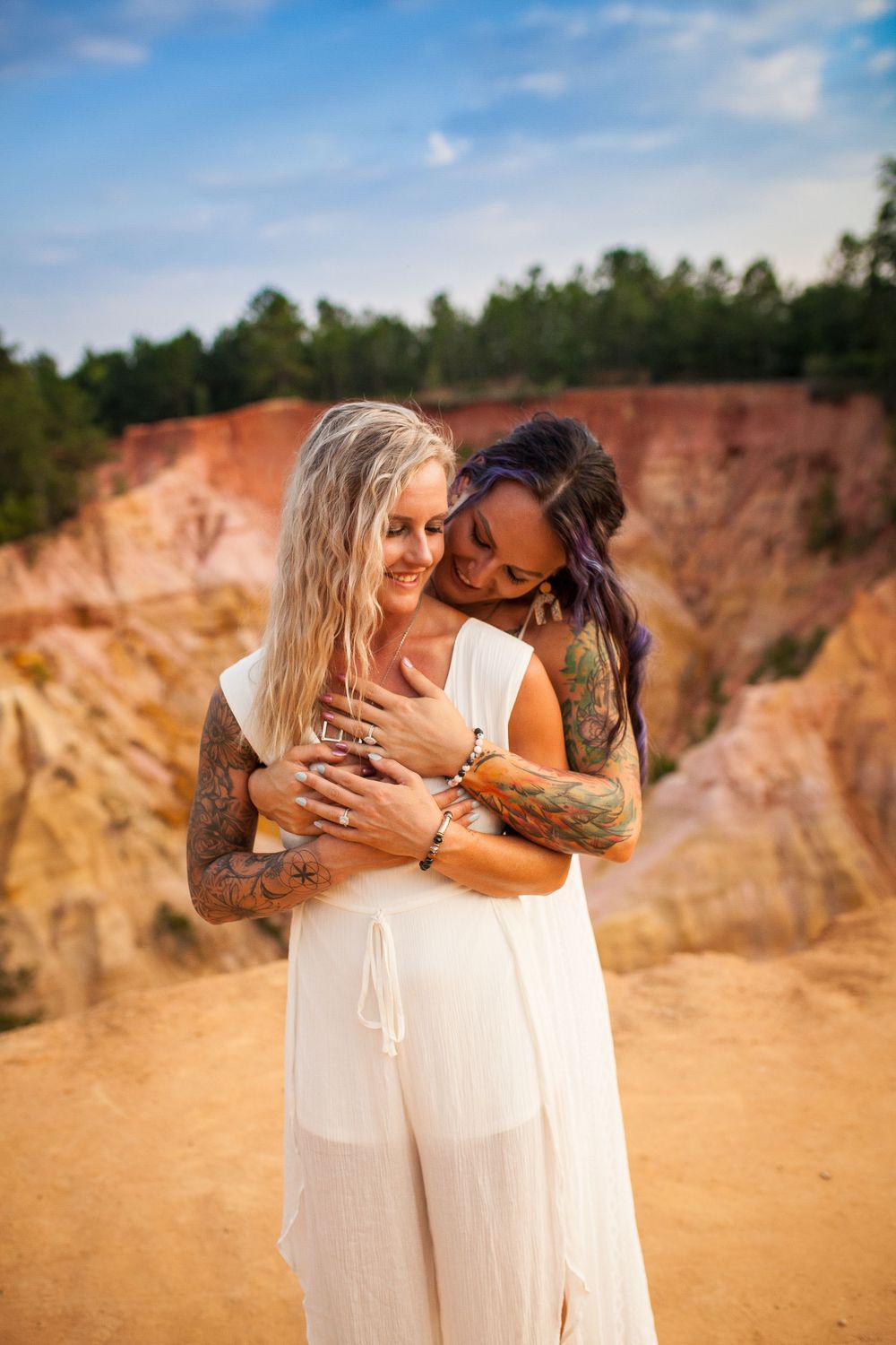 Couple embracing at scenic quarry with colorful tattoos and white outfits.