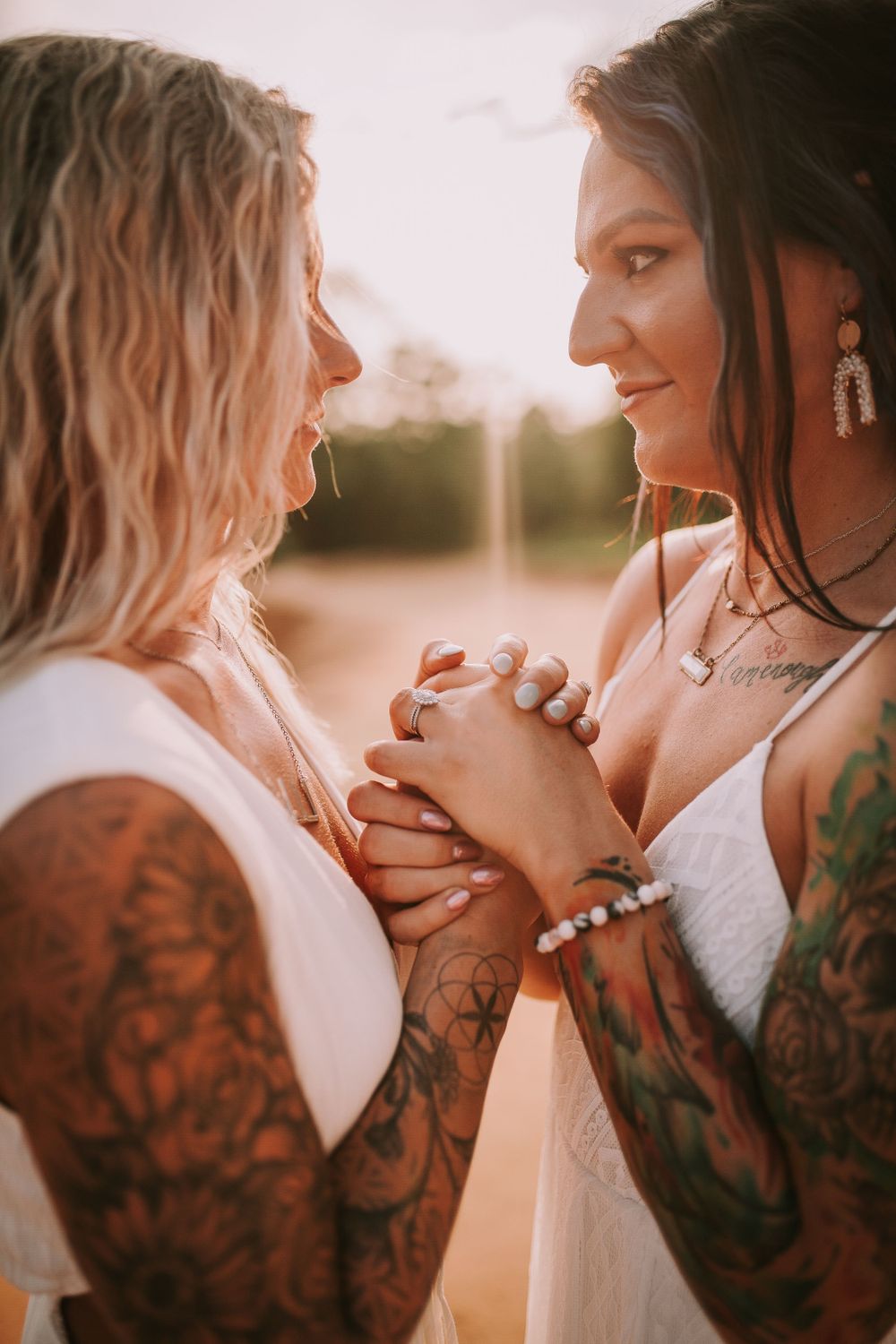Intimate moment between couple with tattoos holding hands at sunset.