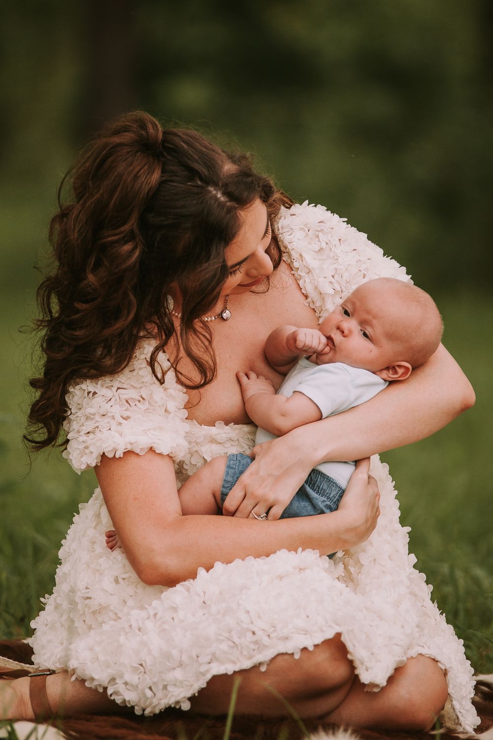 A tender moment between parent and baby on grassy ground in white lace dress.