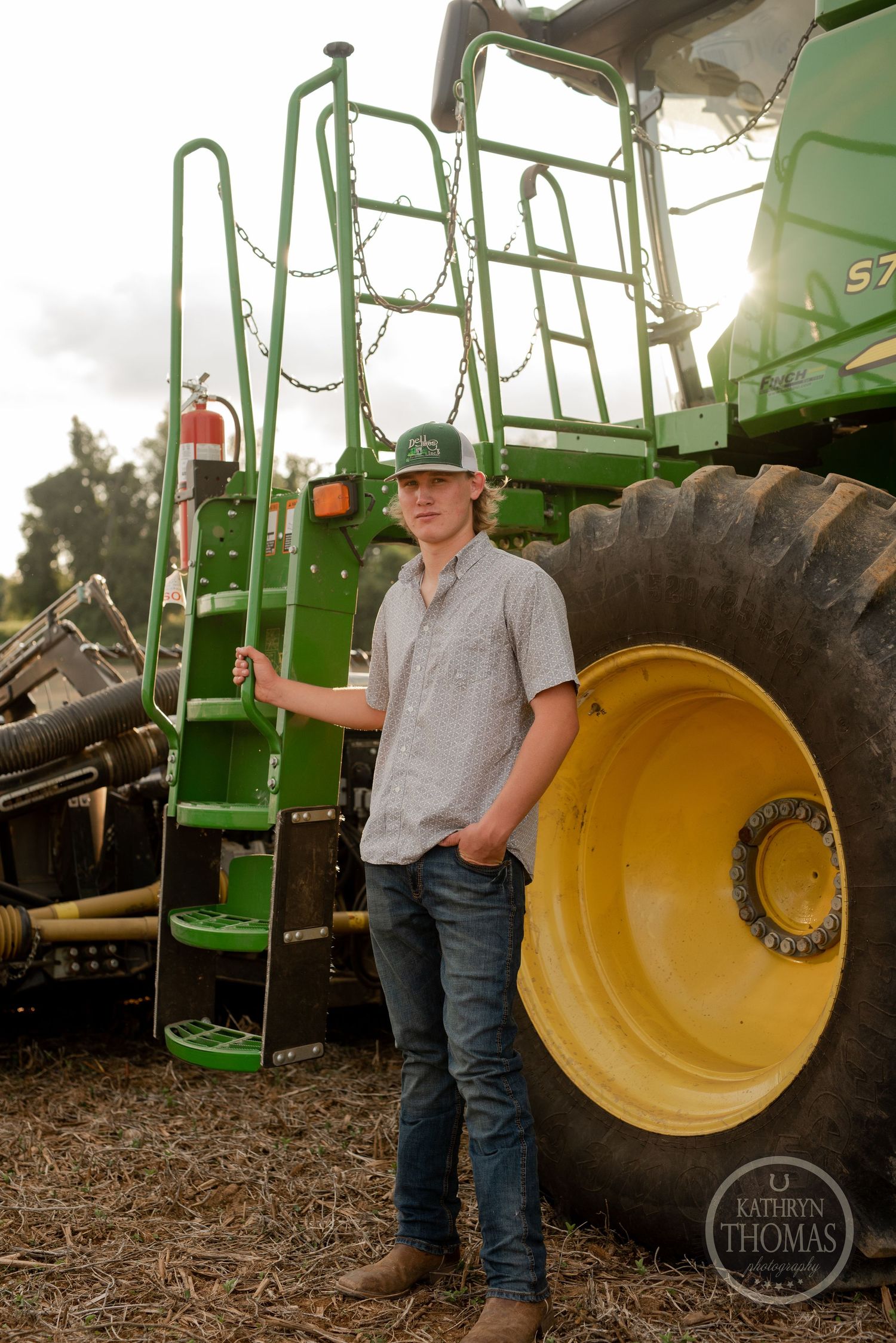 Farmer stands beside large agricultural equipment with climbing ladder in golden sunlight.