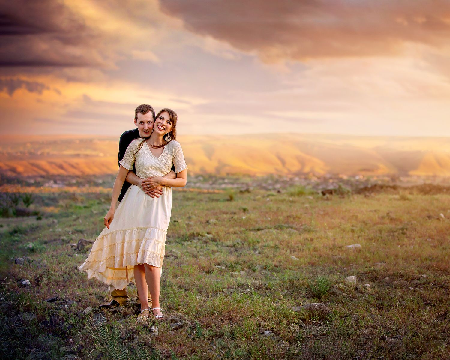 Couple hugging and smiling on a mountain top at sunset