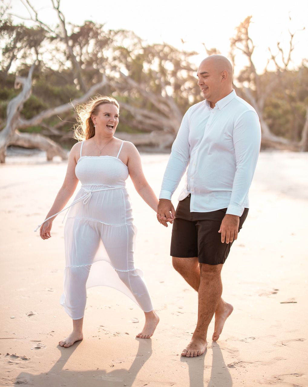 Happy couple sharing a candid moment while walking barefoot on beach at sunset.