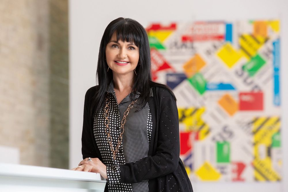 Woman in business attire smiling against colorful modern art wall display.