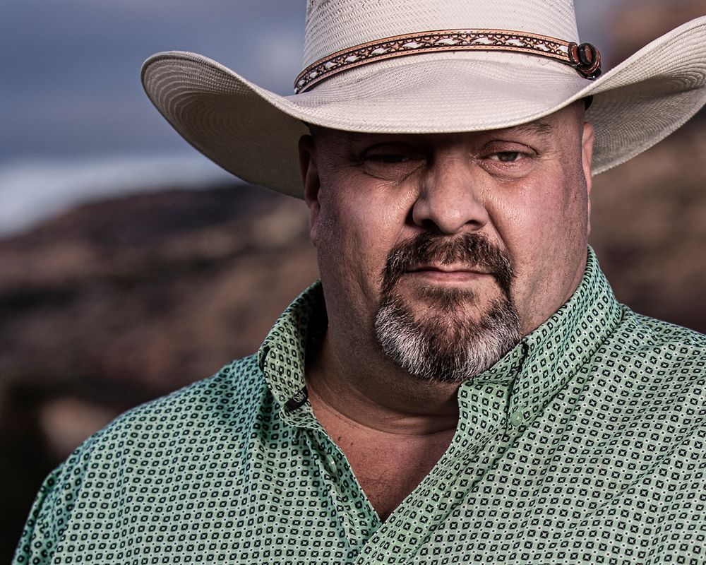 Portrait of rancher wearing cowboy hat and green checkered shirt against desert landscape.