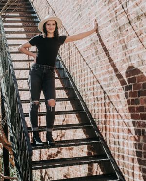 Urban fashion shoot on black metal fire escape stairs against brick wall.