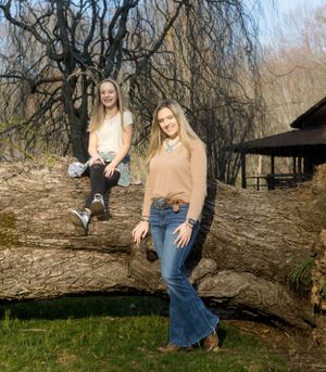 Two people sit and pose playfully on a fallen tree trunk in a natural outdoor setting.
