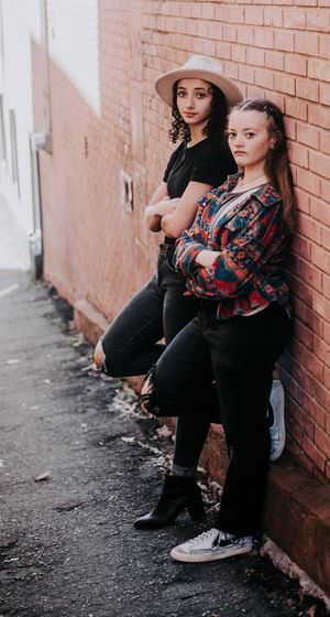 People in casual attire and hats pose against a rustic brick wall.