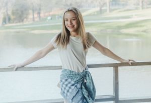 A person in casual attire poses on a lakeside deck with arms outstretched.