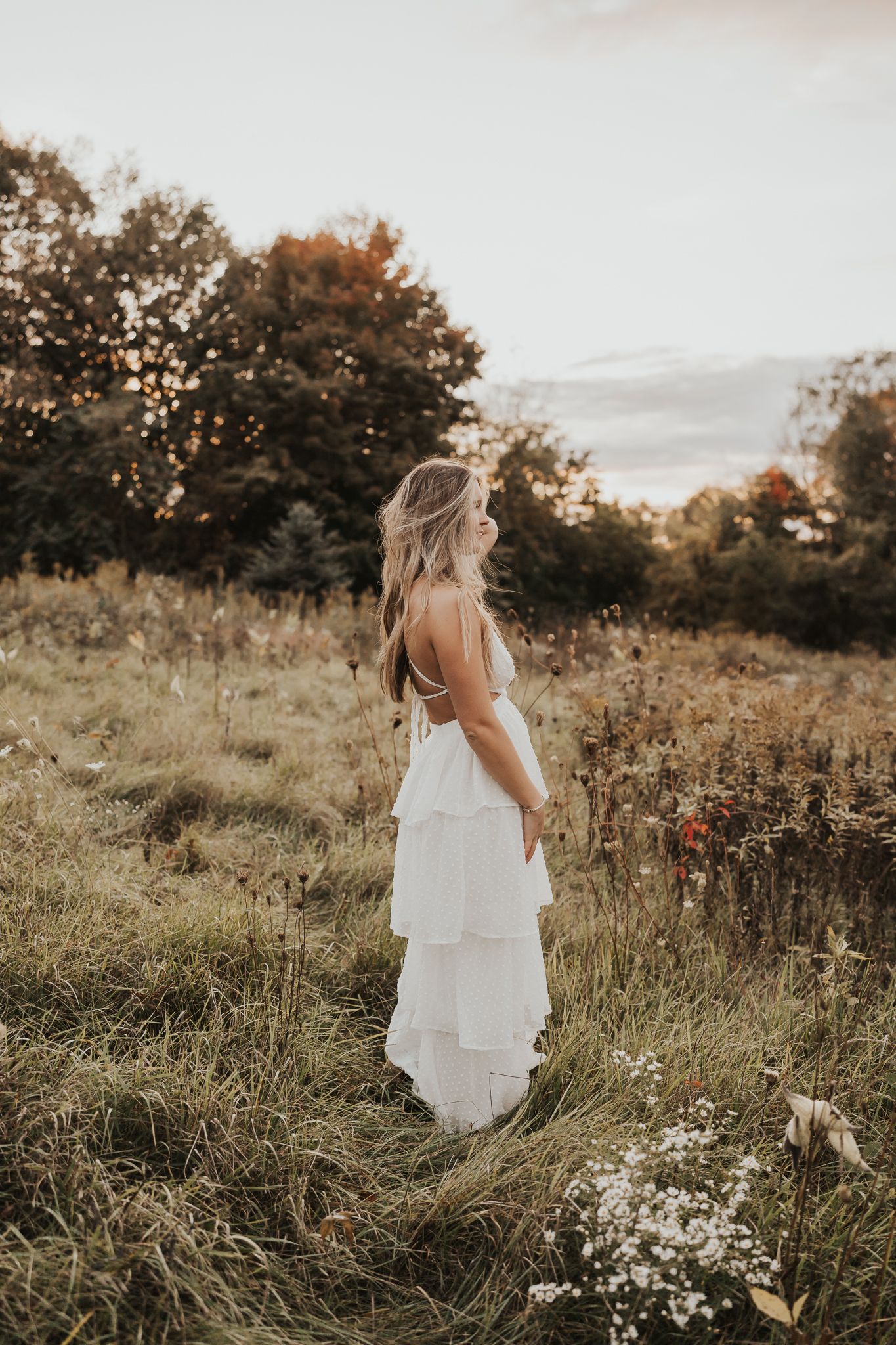 A flowing white dress moves gracefully through a golden field at sunset for senior photograph taken in Pulaski MI.