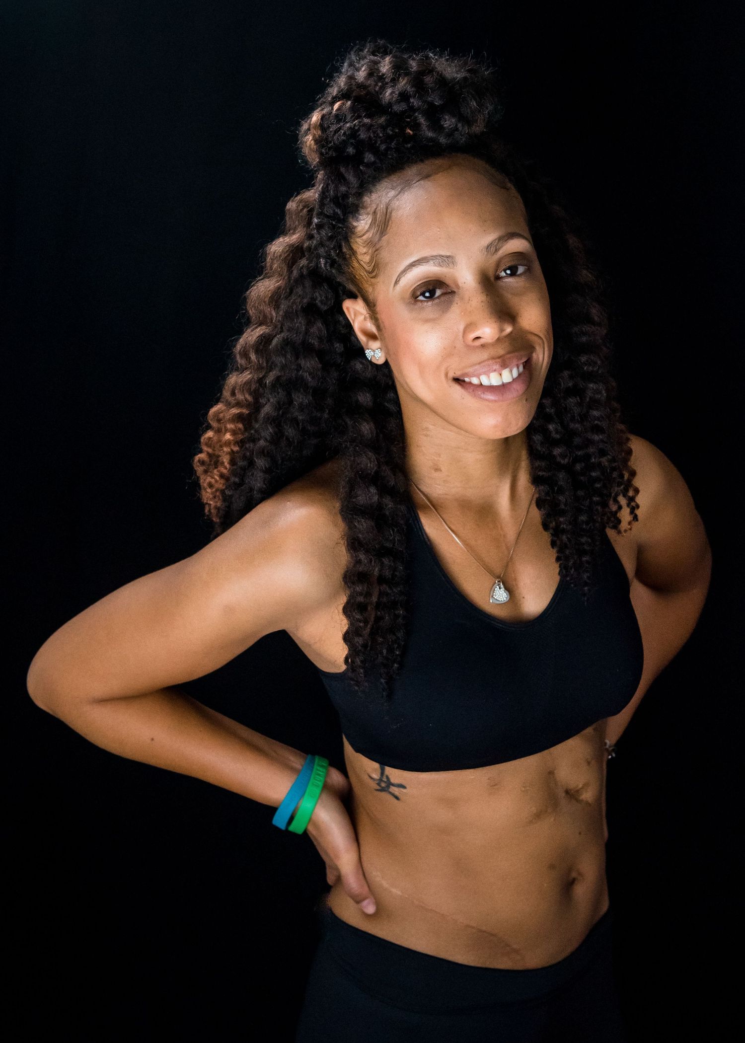 Athletic portrait of fitness model in black sports attire against dark background.
