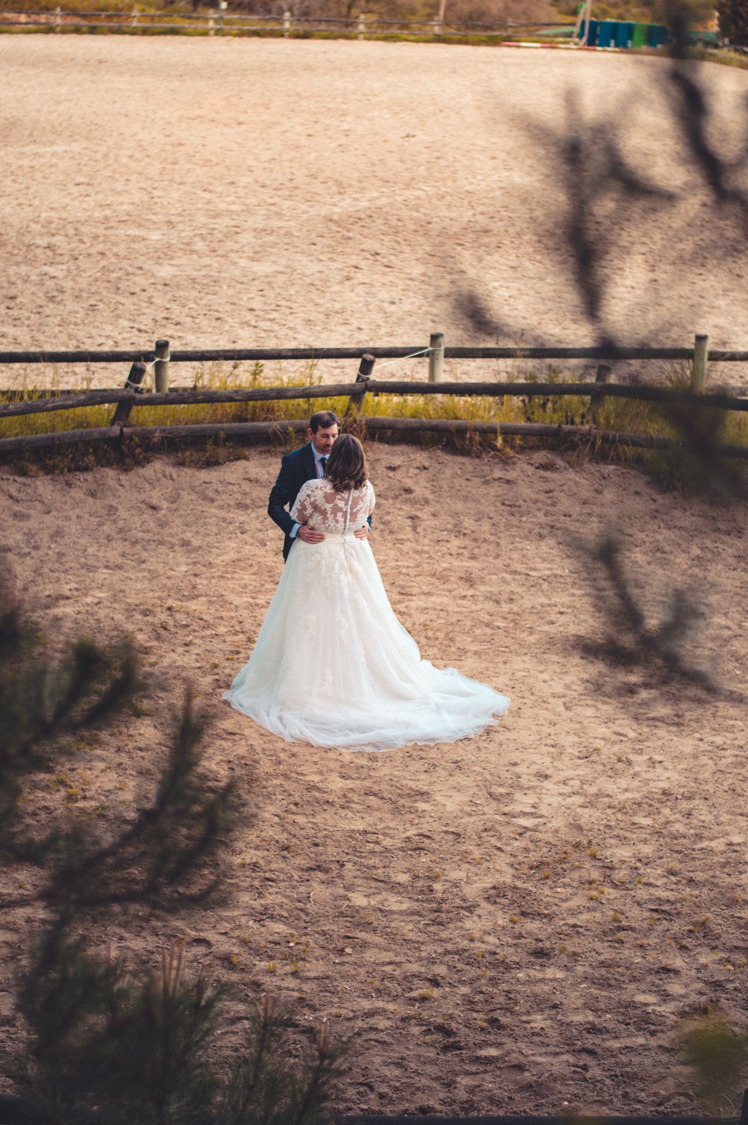 Aerial view of wedding couple standing in rustic fenced arena during countryside celebration.