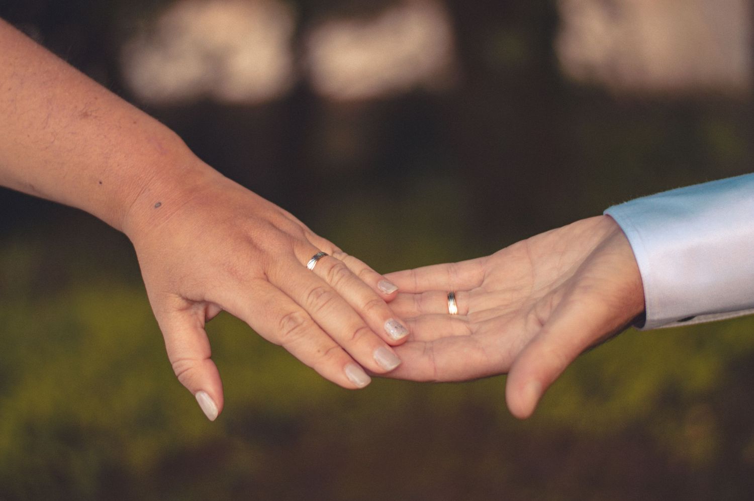 Close-up of newlywed couple's hands with wedding rings in natural outdoor setting.