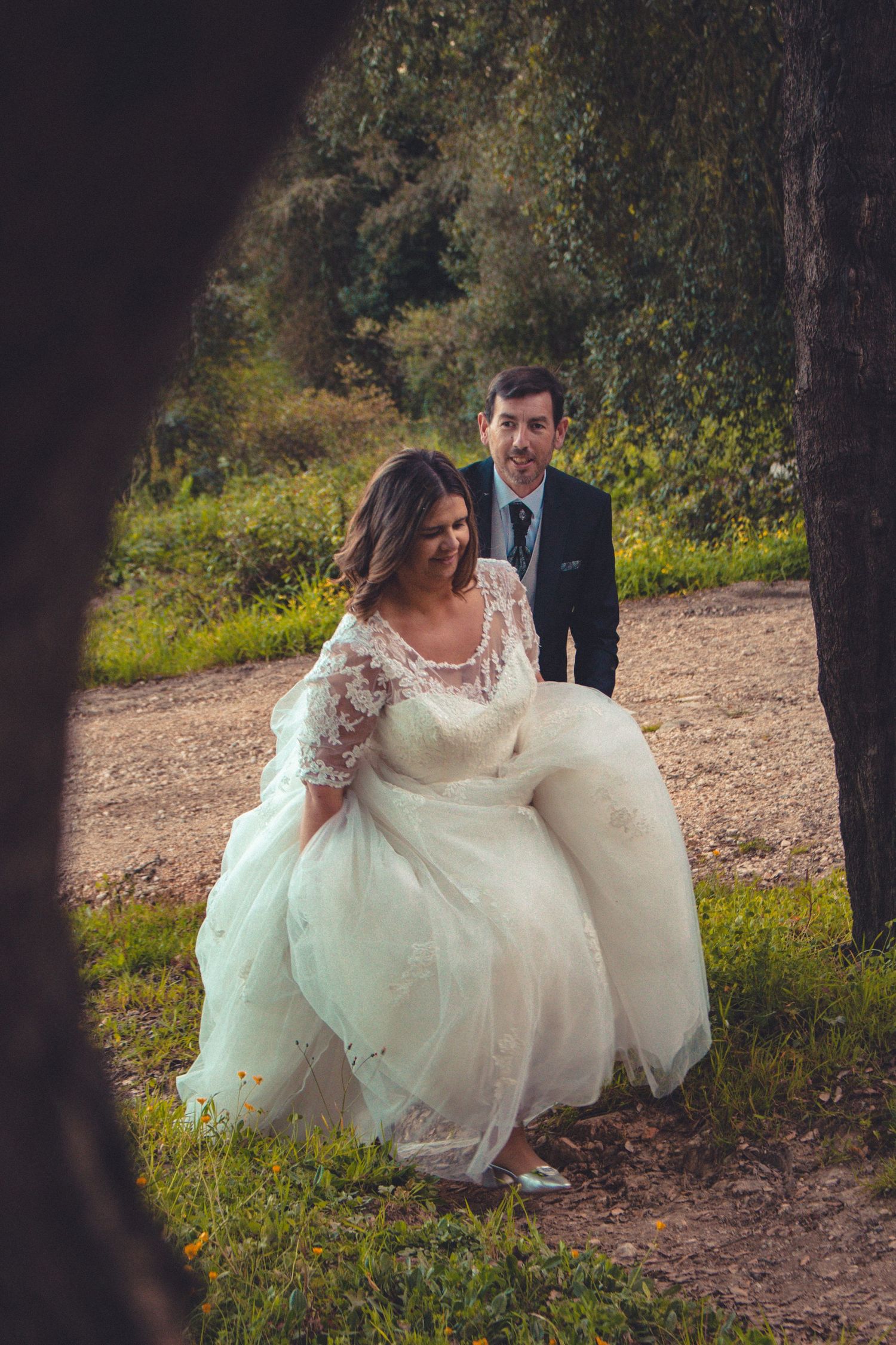 Bride in flowing white dress walking through a wooded area with fallen leaves.