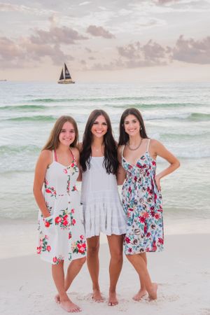 3 girls standing on Panama City Beach Florida with a sunset & sailboat in the background