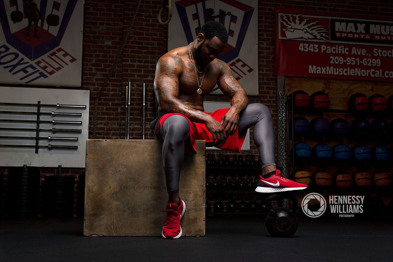 Athletic figure in red and gray workout gear sits contemplatively in gym setting.