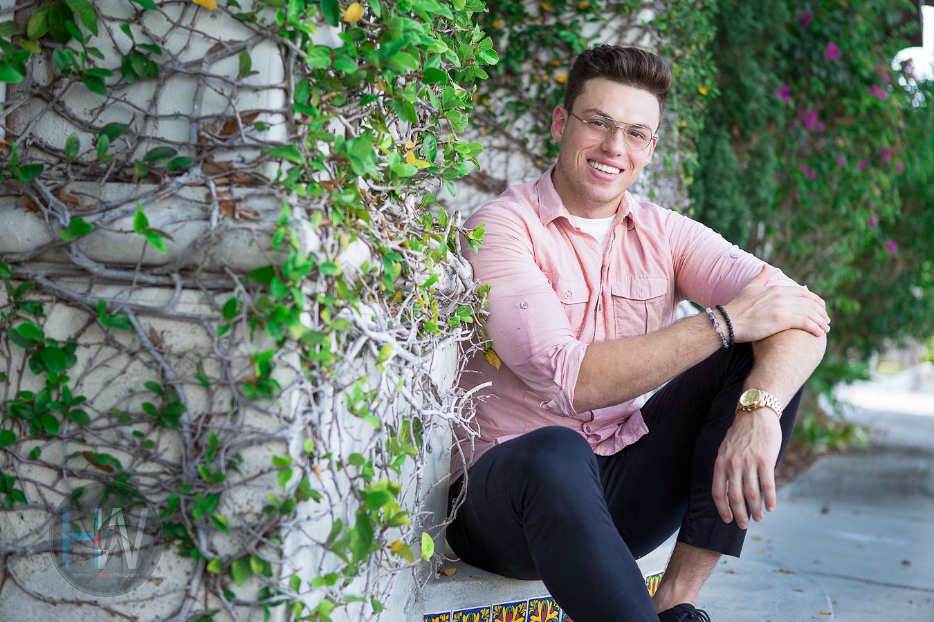 Portrait of person in pink button-down shirt sitting against vine-covered stone wall.