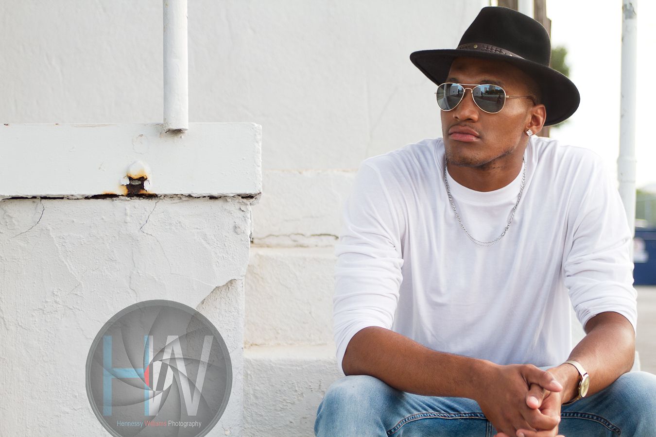 A casual street style portrait with white t-shirt, hat and sunglasses against white wall.
