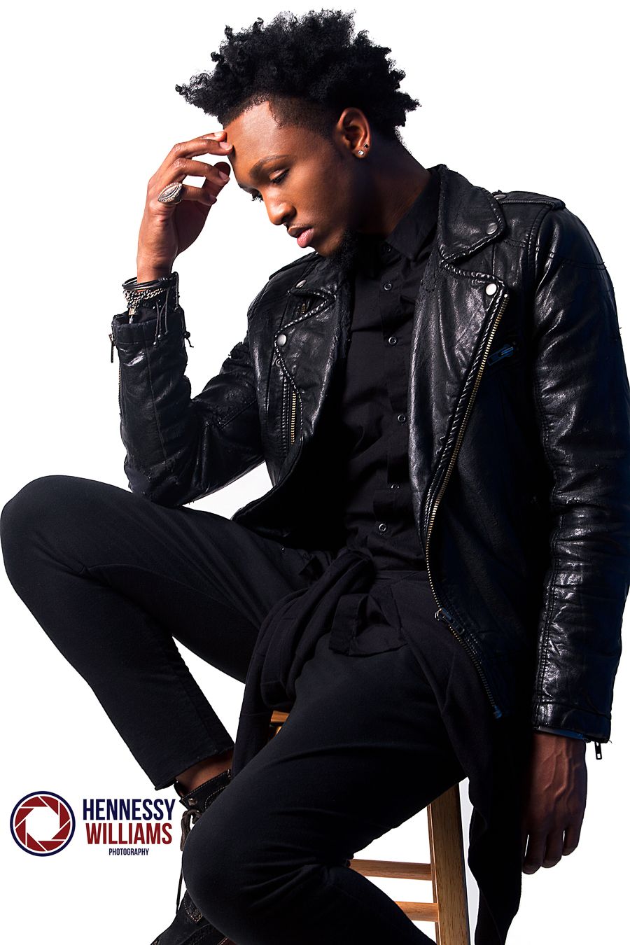 A moody fashion portrait in all black with leather jacket against studio backdrop.
