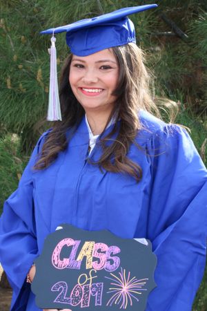 Graduate in blue cap and gown holding Class of 2011 sign during commencement celebration.