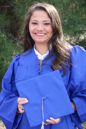 Graduate wearing bright blue graduation gown holds diploma while smiling outdoors.
