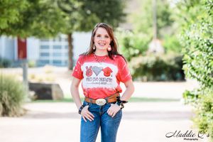 A casual outdoor portrait featuring a red graphic t-shirt and jeans against a natural background.
