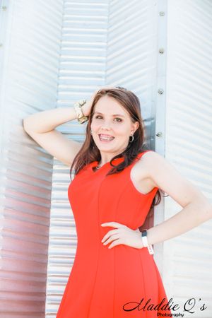 Portrait in a bright red sleeveless dress against a white striped architectural background.