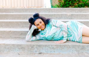 Person in mint patterned top lounging on concrete steps outdoors.