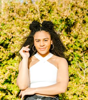 Person in white halter top poses against sunny yellow-green foliage background.