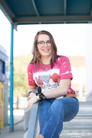 Casual portrait in a graphic t-shirt and jeans while sitting on a railing under a blue awning.