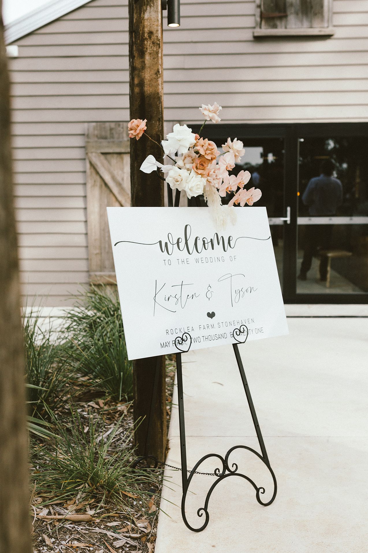 Elegant welcome signs on iron stands outside a white weatherboard building.