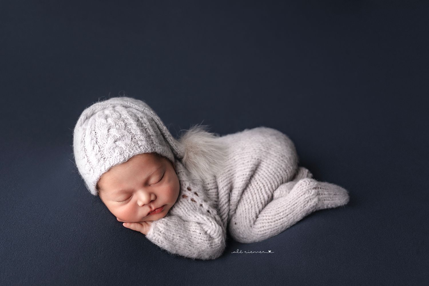 Sleeping newborn wearing knit hat and sweater on dark background.