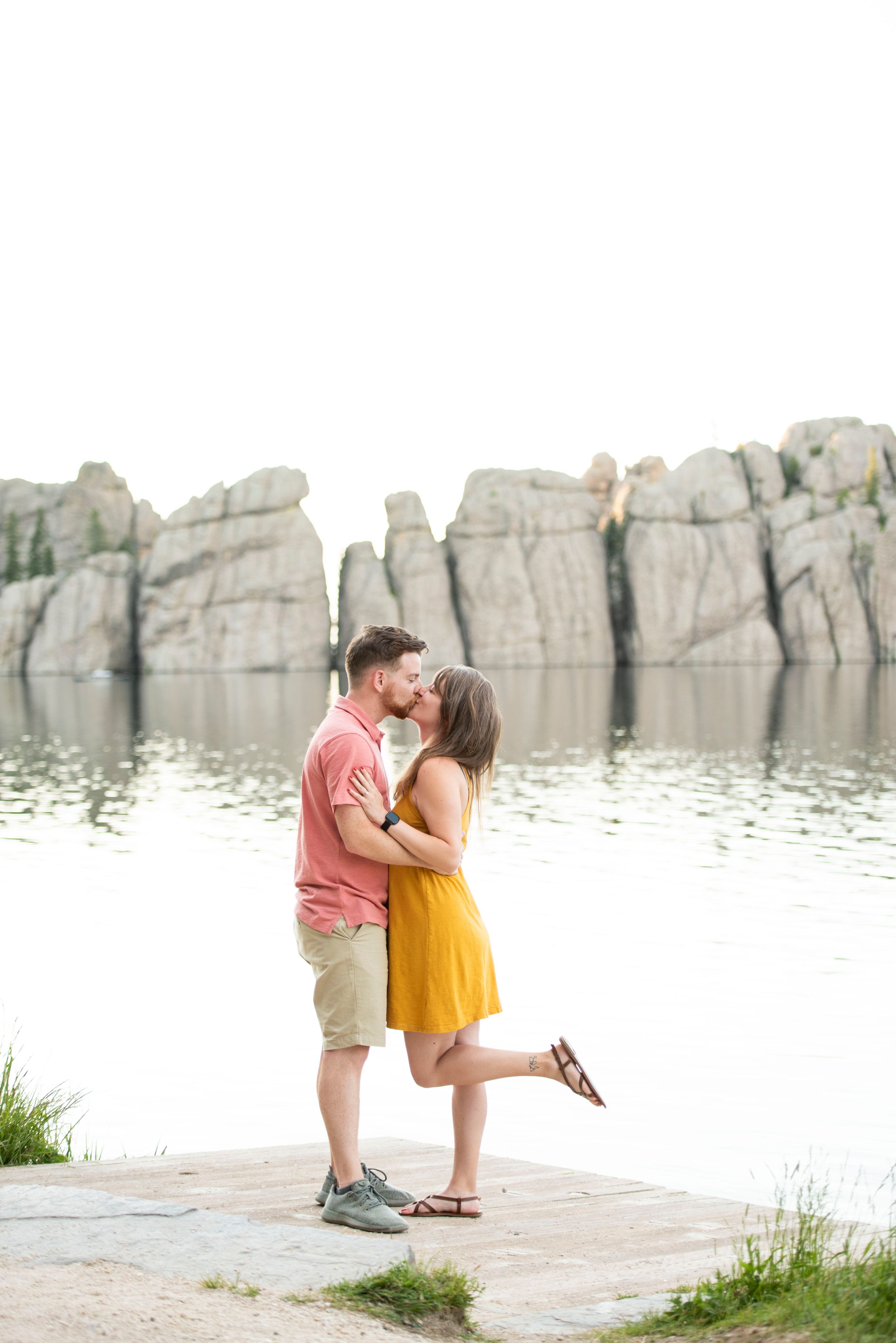 A romantic moment captured by a rocky waterfront with dramatic cliffs in the background.