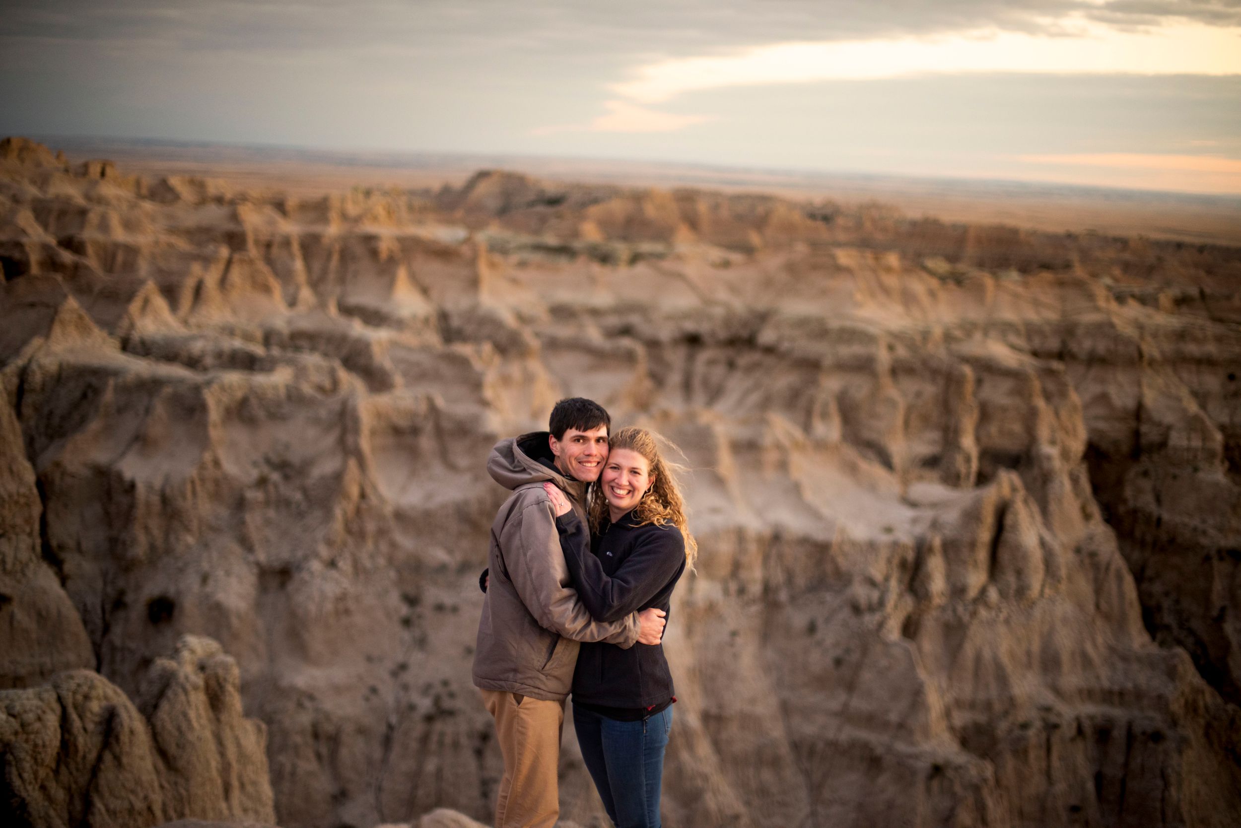 A romantic couple embracing against dramatic desert cliffs at sunset.