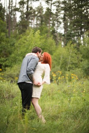 Couple sharing intimate moment in a wildflower meadow with pine trees.