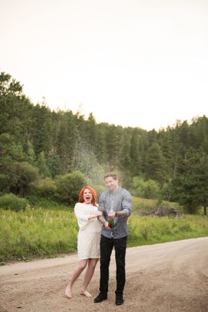 Playful couple dancing on a dirt road surrounded by forest.