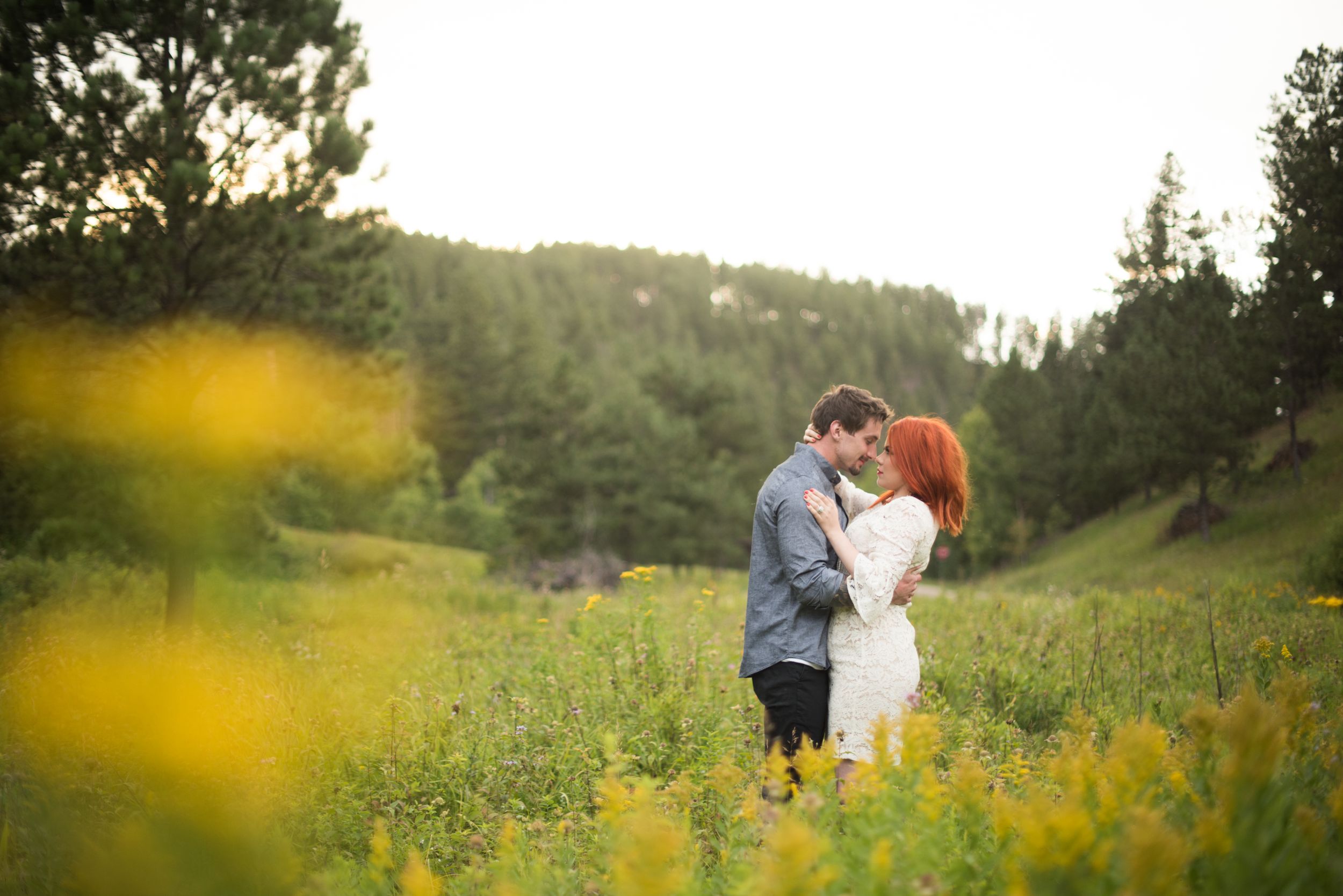 Couple embracing in a field of yellow wildflowers at golden hour.