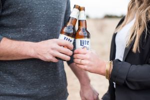 Hands exchanging beer bottles in casual outdoor setting.