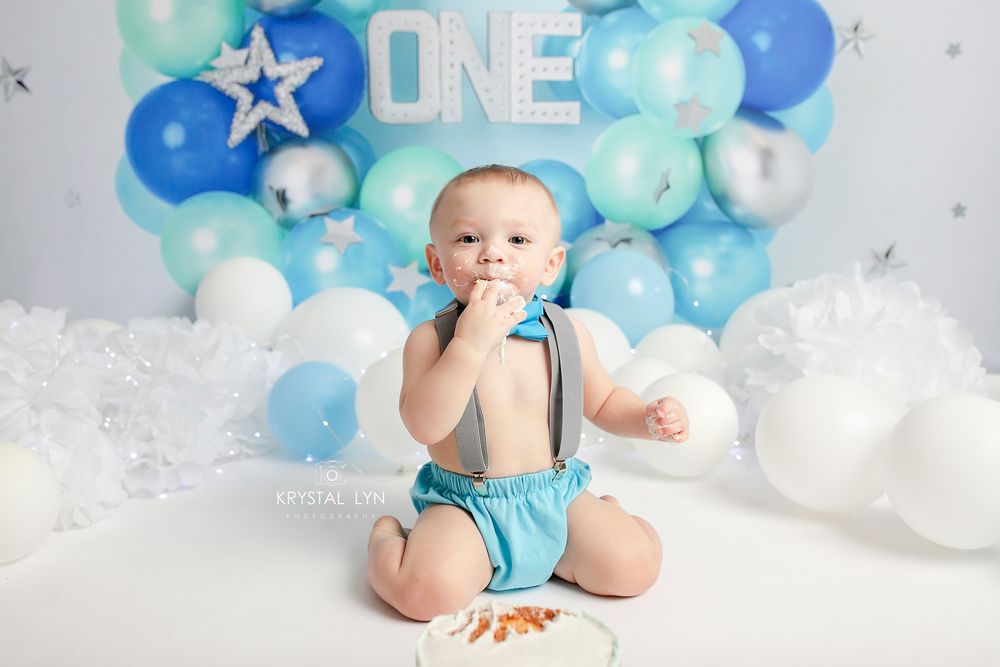One year old cake smash enjoying his cake on a blue and white birthday set up
