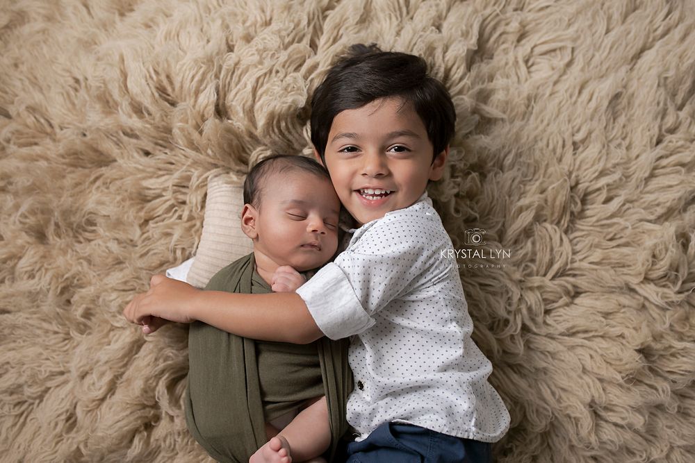 Happiest big brother cuddling his new brother on beige flokati