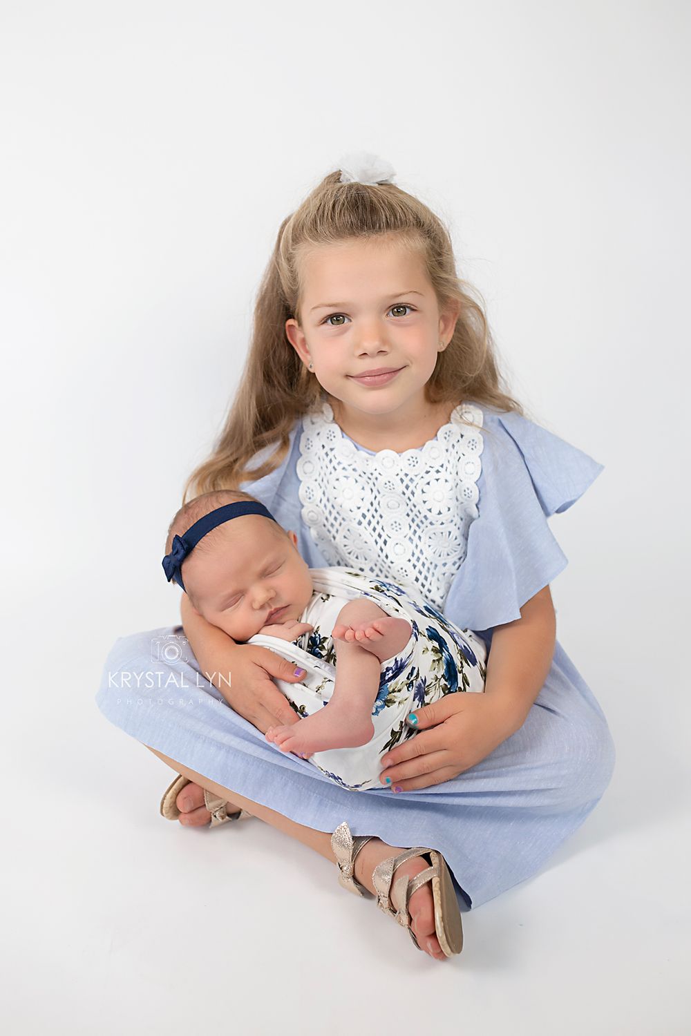 Responsible big sister posing with her baby sister, both wearing blue