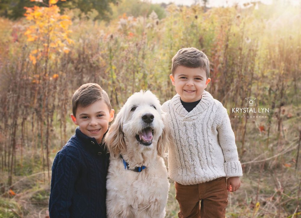 Two siblings pose with their family dog in the tall grassy fields
