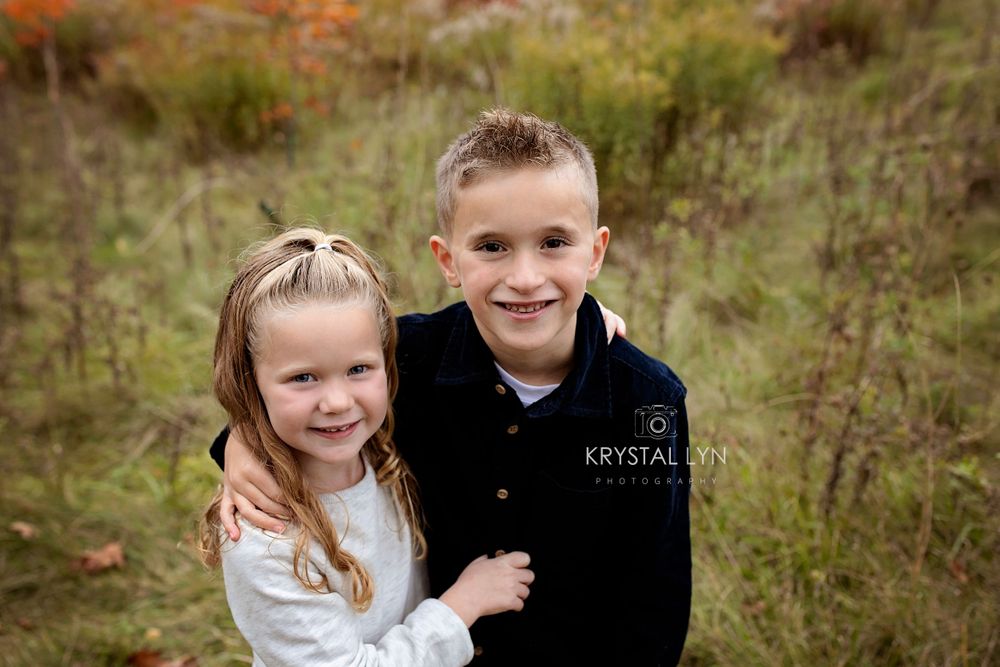 Brother with his arm around his little sister, big smiles from both of them