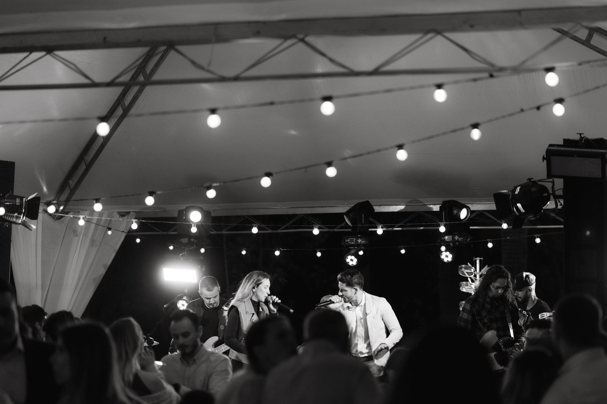 Black and white reception scene with string lights illuminating a crowded dance floor.