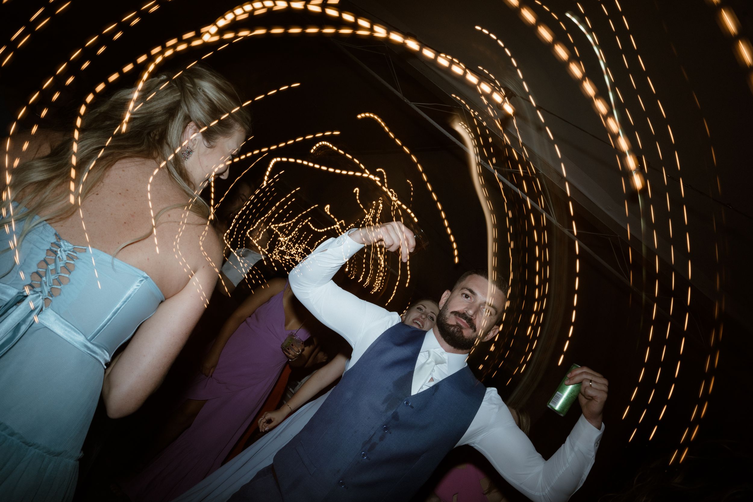 Abstract spiral light trails capture wedding party dancing at night reception.