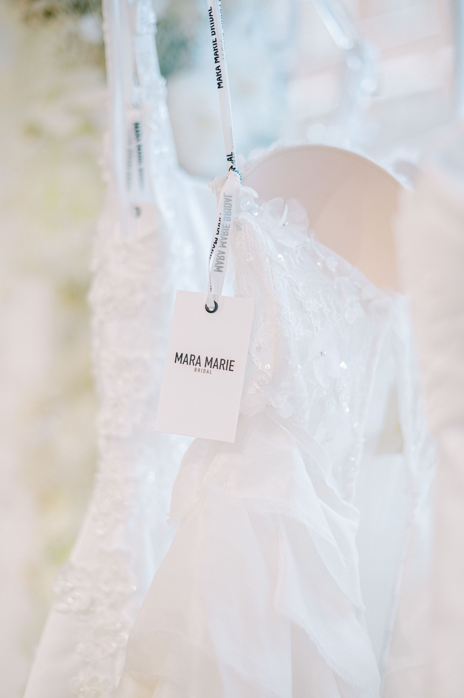 Delicate white wedding dress hangers with Mara Marie branding in soft focus.