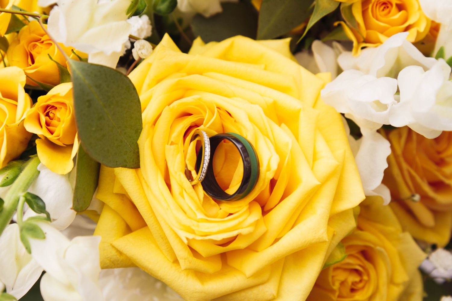 Close-up of a vibrant yellow rose with a wedding ring nestled in its petals.