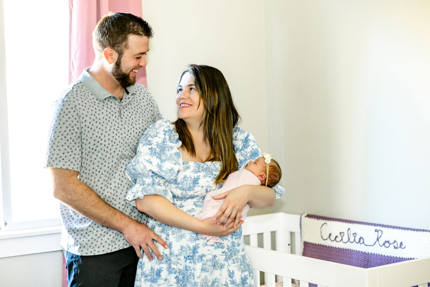 Parents hold their new baby girl and smile at each other in her nursery during newborn photos in Colorado Springs.