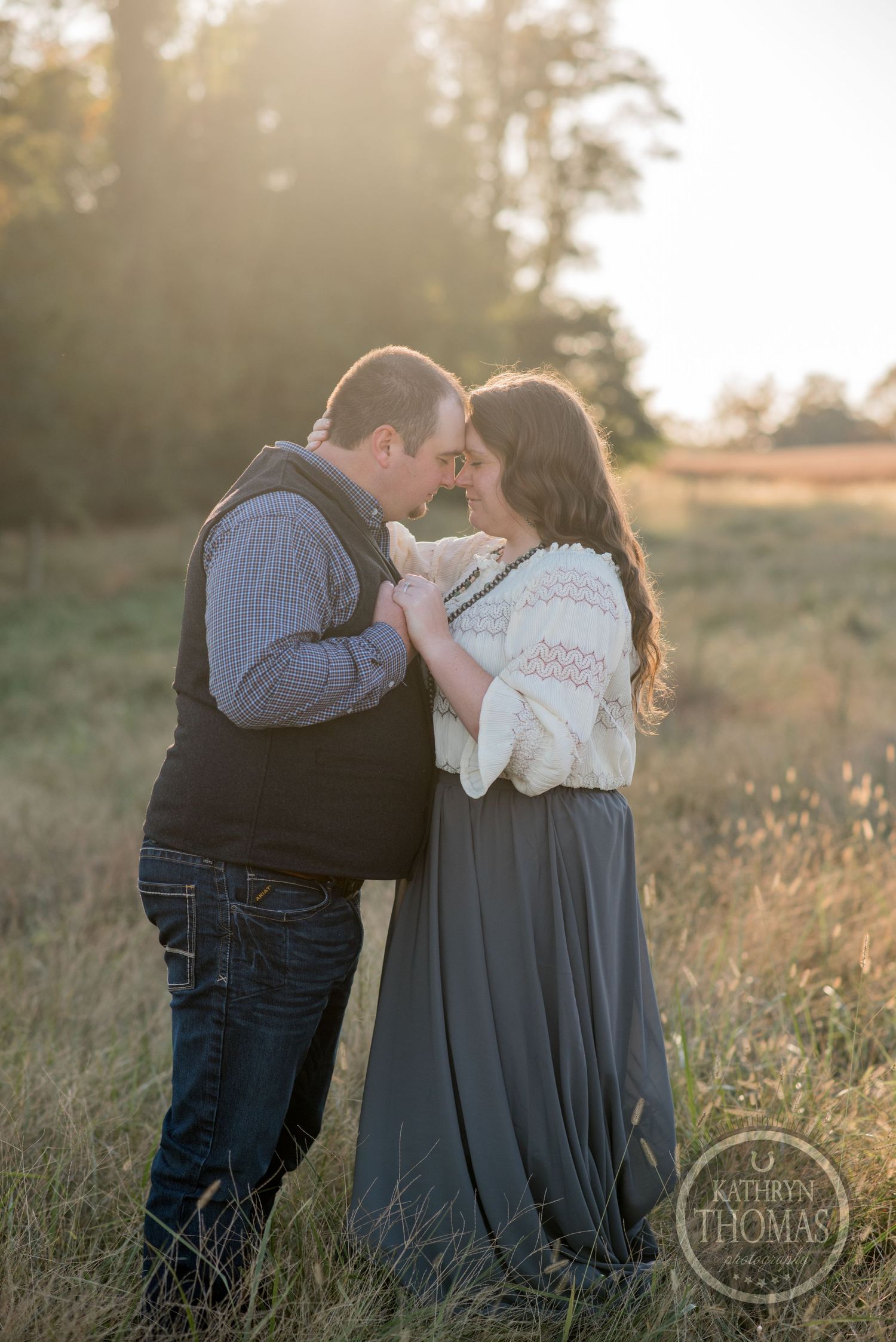 A tender moment between a couple in casual attire during golden hour in a field.