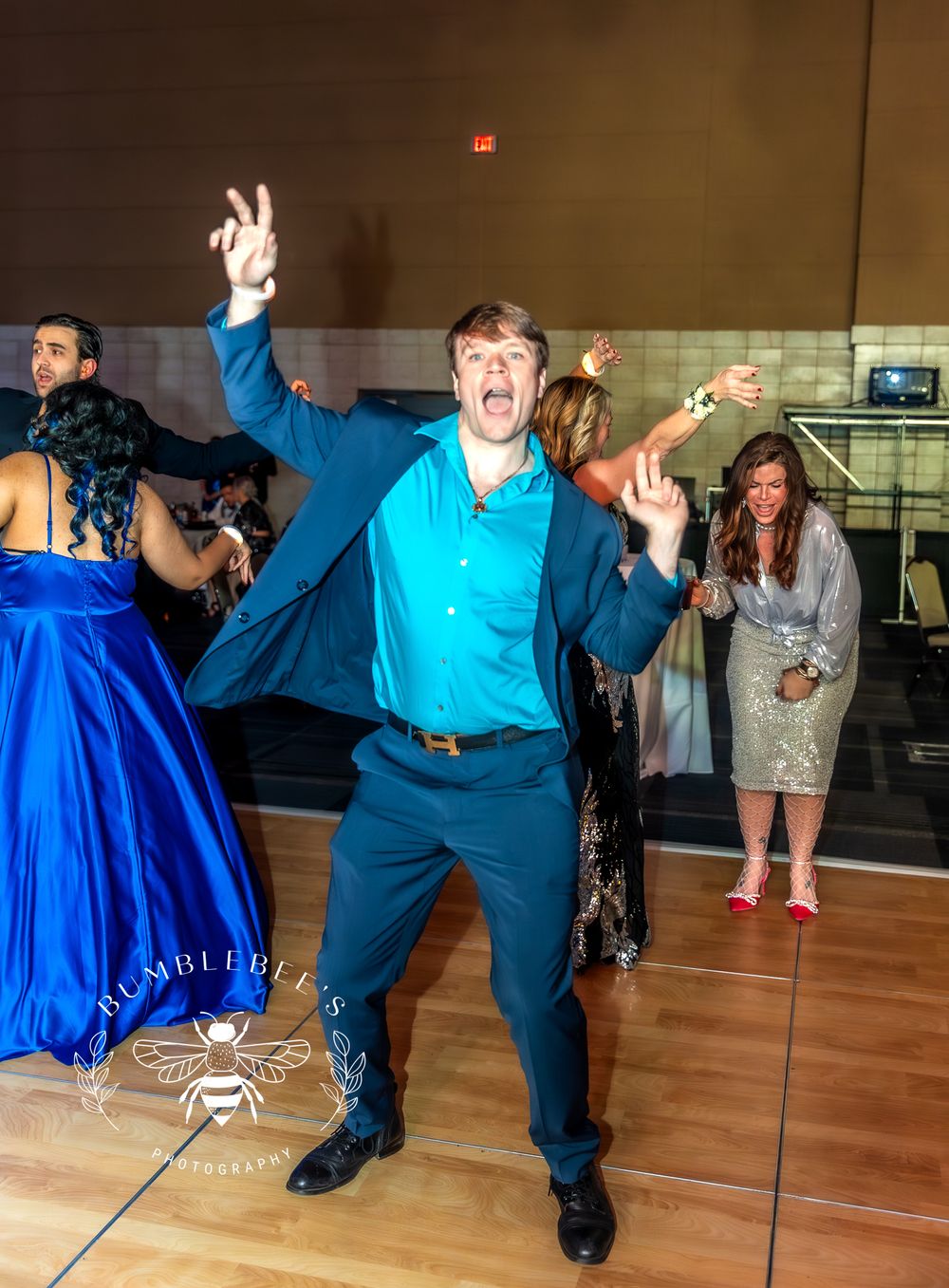 Party guest in blue suit showing energetic dance moves on wooden floor at formal event.