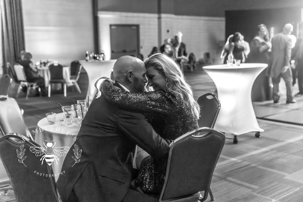 A black and white candid photo captures an intimate moment between guests at a formal event.